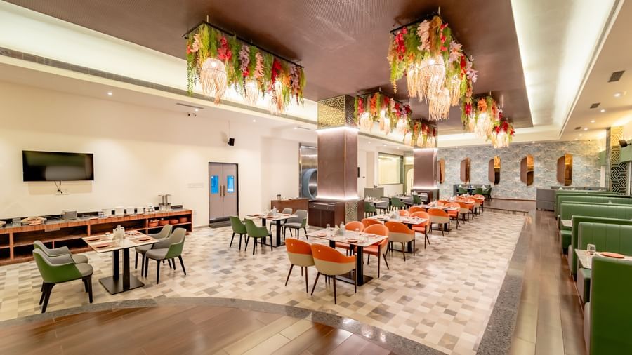A rstaurant space with orange and green seating and intricate ceiling decorations | Pravasa Hotel, Vijayapura