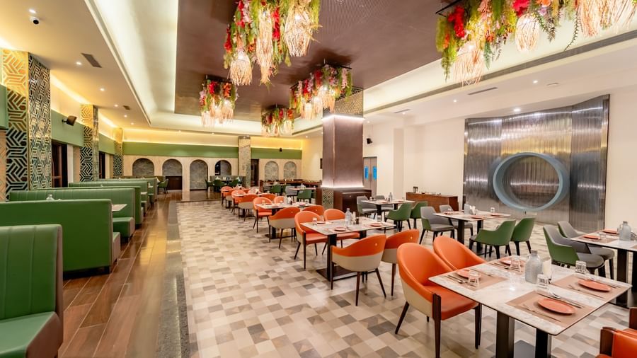 Dining area with green sofas and orange chairs and decorative hanging elements | Pravasa Hotel, Vijayapura