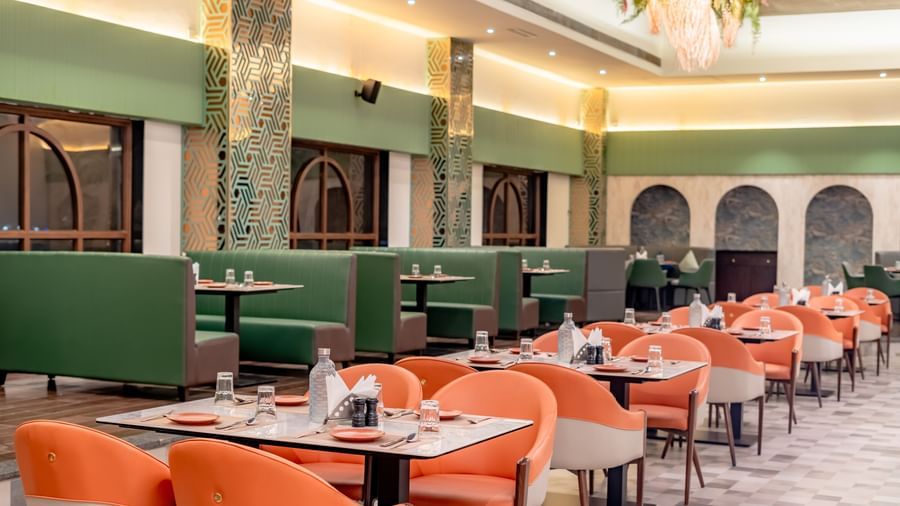 A dining area with green and orange chairs and decorative hanging elements | Pravasa Hotel, Vijayapura