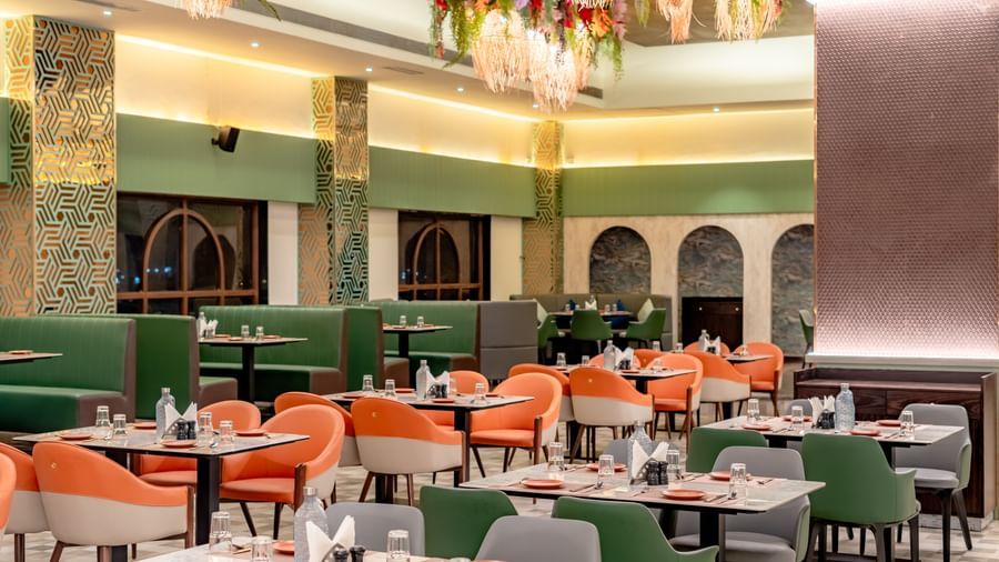 Dining area with green and orange chairs and decorative hanging elements | Pravasa Hotel, Vijayapura