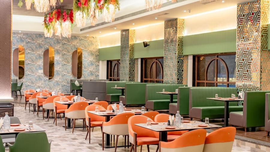 Dining area with green sofas and orange chairs | Pravasa Hotel, Vijayapura