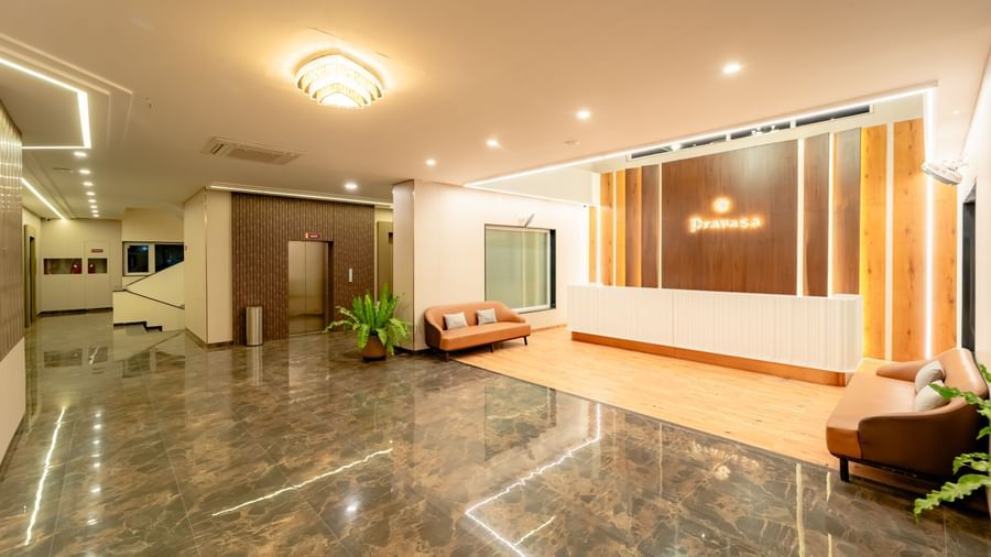 A well-lit waiting lounge with light-colored sofas and a large potted plant | Pravasa Hotel, Vijayapura