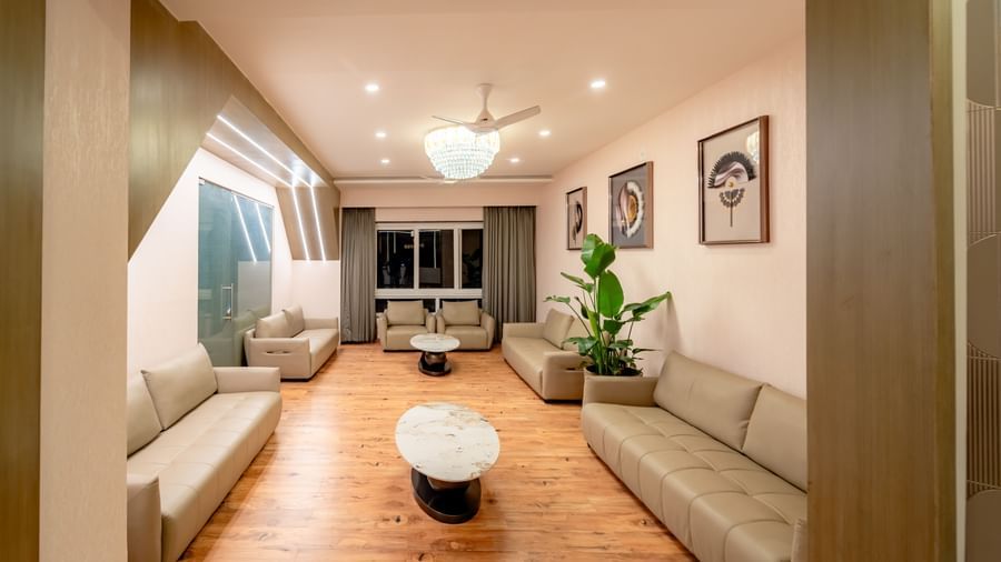 A well-lit waiting lounge with light-colored sofas and a large potted plant | Pravasa Hotel, Vijayapura