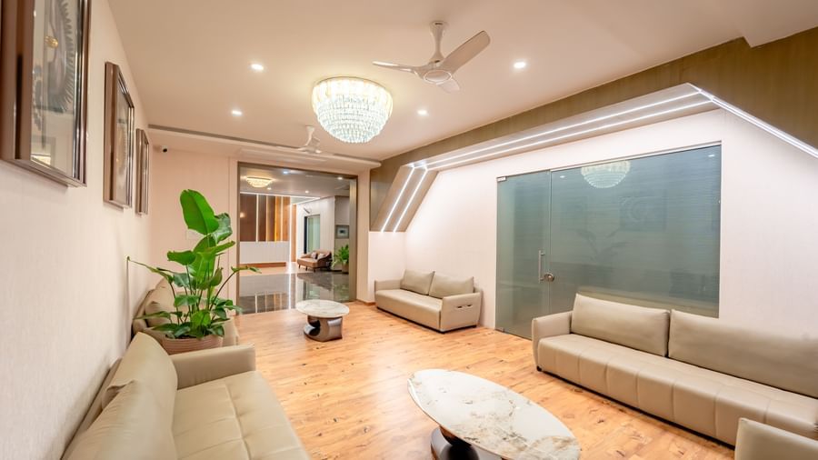 Well-lit waiting lounge with light-colored sofas and a large potted plant | Pravasa Hotel, Vijayapura