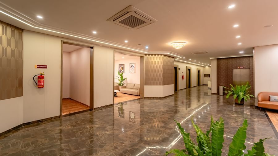 Hotel lobby with a front desk, elevators, and warm ambient lighting | Pravasa Hotel, Vijayapura Entrance of Pravasa Hotel's reception area with brown sofas and plant decor | Pravasa Hotel, Vijayapura