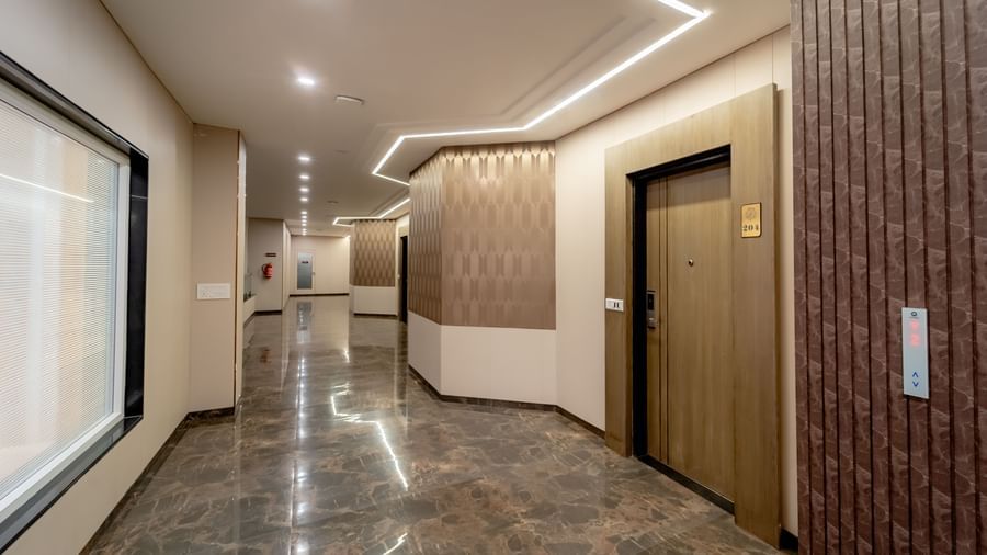 Spacious hotel corridor featuring an elevator, and warm ambient lighting | Pravasa Hotel, Vijayapura