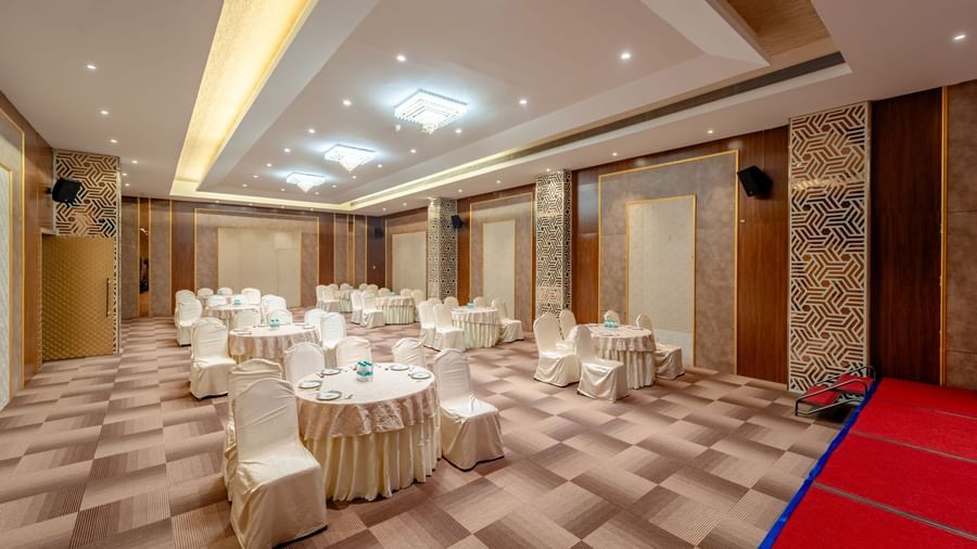 Event hall configured with round tables and draped chairs for a banquet | Meetings & Events | Pravasa Hotel, Vijayapura