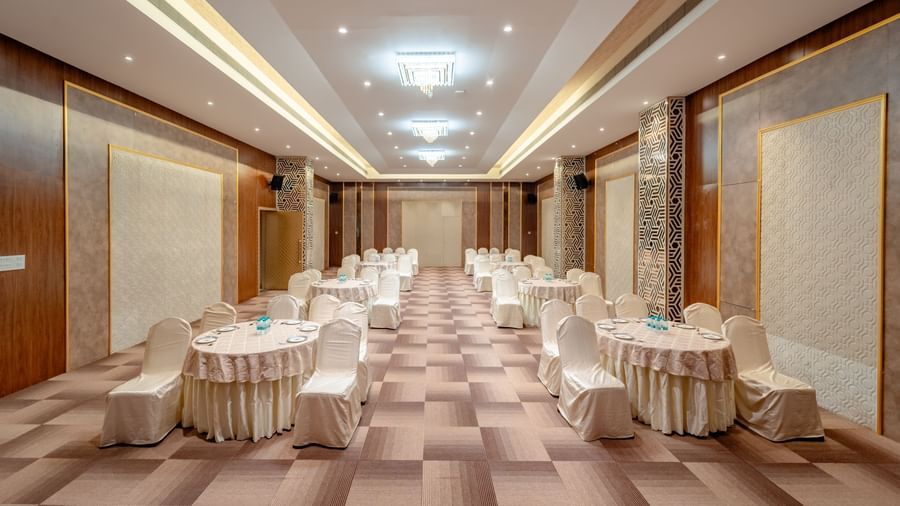 A conference room with round tables and beige chairs, ready for an event | Meetings & Events | Pravasa Hotel, Vijayapura