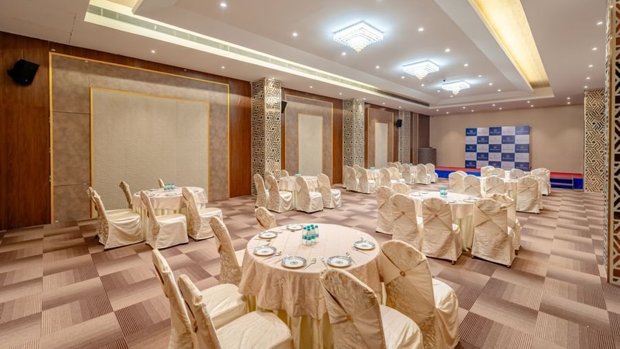 A banquet hall with round tables and beige chairs | Meetings & Events | Pravasa Hotel, Vijayapura