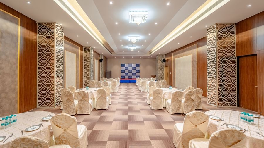 Meeting room with multiple rows of chairs facing a stage area | Meetings & Events | Pravasa Hotel, Vijayapura