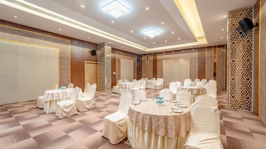 Spacious banquet hall with round tables and elegant chair covers | Meetings & Events | Pravasa Hotel, Vijayapura