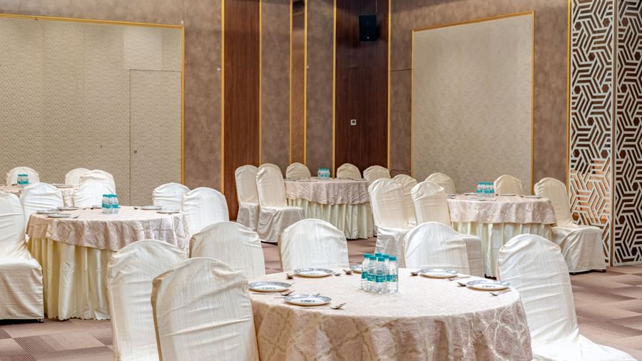 A banquet hall with round tables and elegant chairs | Meetings & Events | Pravasa Hotel, Vijayapura