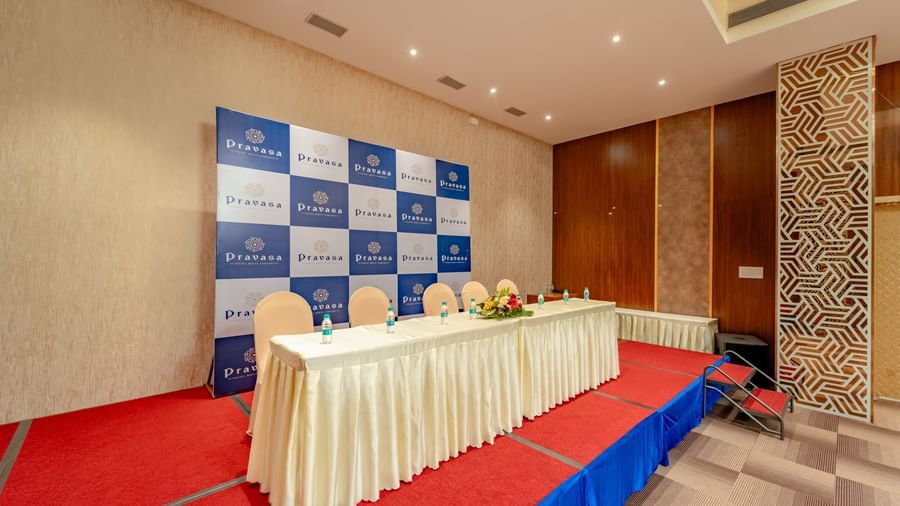 Stage area in the event hall with a table draped in white and blue backdrop | Meetings & Events | Pravasa Hotel, Vijayapura