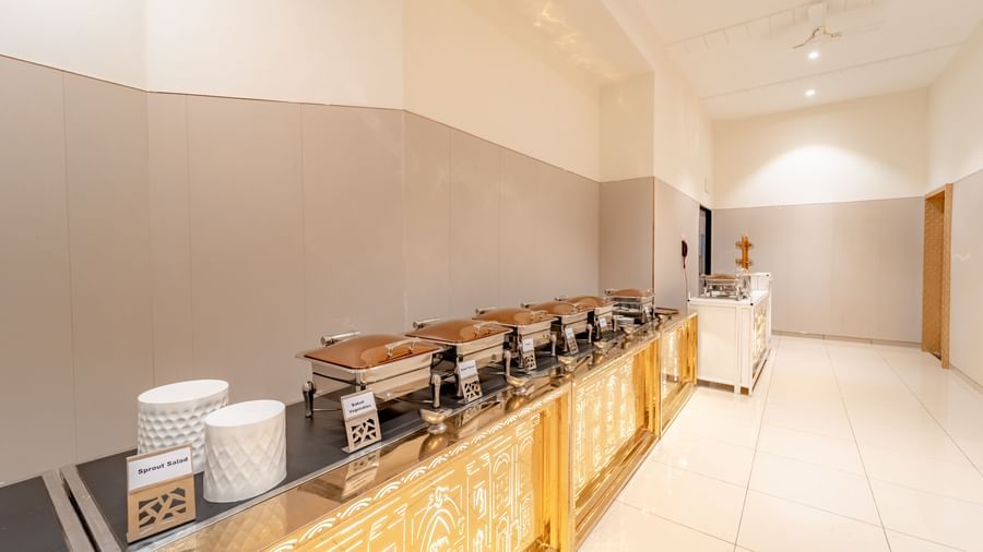  A long buffet table with chafing dishes and decorative white stools | Meetings & Events | Pravasa Hotel, Vijayapura