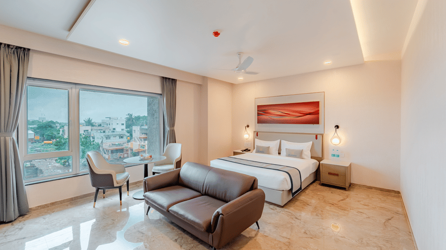  A spacious room with a king-size bed, a sofa, and a city view | Studio Suite | Pravasa Hotel, Vijayapura