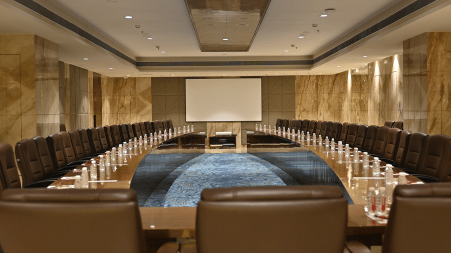 The professional boardroom setup of Allure hall featuring an extended table facing a presentation screen at Praveg's Grand Eulogia, Ahmedabad.