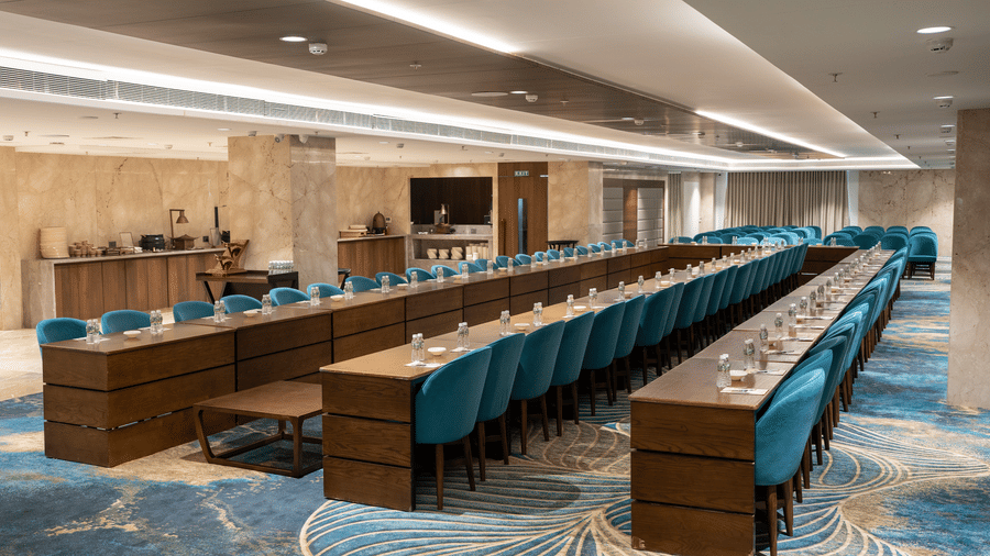 A large conference hall arranged in a theatre setting with teal chairs and a blue patterned carpet - Praveg's Grand Eulogia, Ahmedabad
