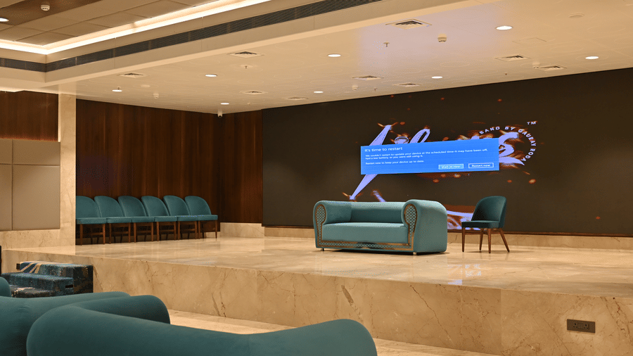 A spacious raised stage featuring a small sofa, an accent chair, and a large display screen in the Eminence banquet hall at Praveg's Grand Eulogia, Ahmedabad.