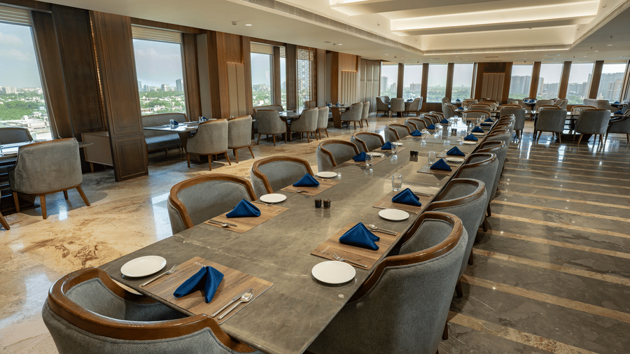 A formal banquet setup with a long stone-top table, grey velvet chairs, and elegant place settings - Praveg's Grand Eulogia, Ahmedabad
