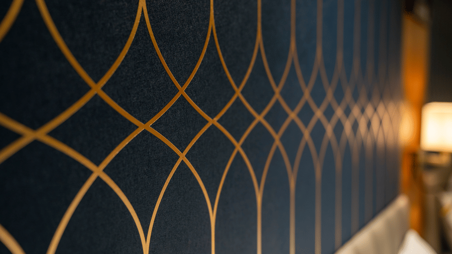 A close-up detail of elegant navy blue wallpaper with a gold geometric pattern in a guest room - Praveg's Grand Eulogia, Ahmedabad