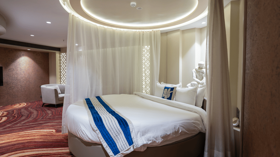 A wide side view of a luxurious circular bed with white linens and blue accents under a halo light - Praveg's Grand Eulogia, Ahmedabad