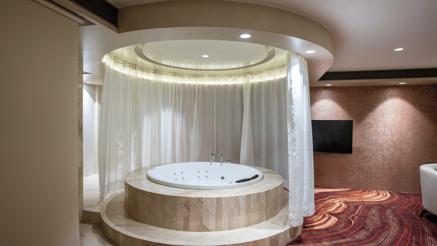 A high-end hotel suite featuring an indoor circular jacuzzi with elegant curtain draping - Praveg's Grand Eulogia, Ahmedabad