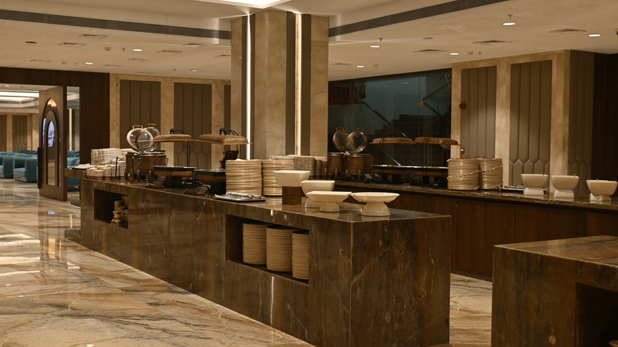 A long wooden buffet counter stands on a glossy marbled floor inside the Marquis banquet hall at Praveg's Grand Eulogia, Ahmedabad.
