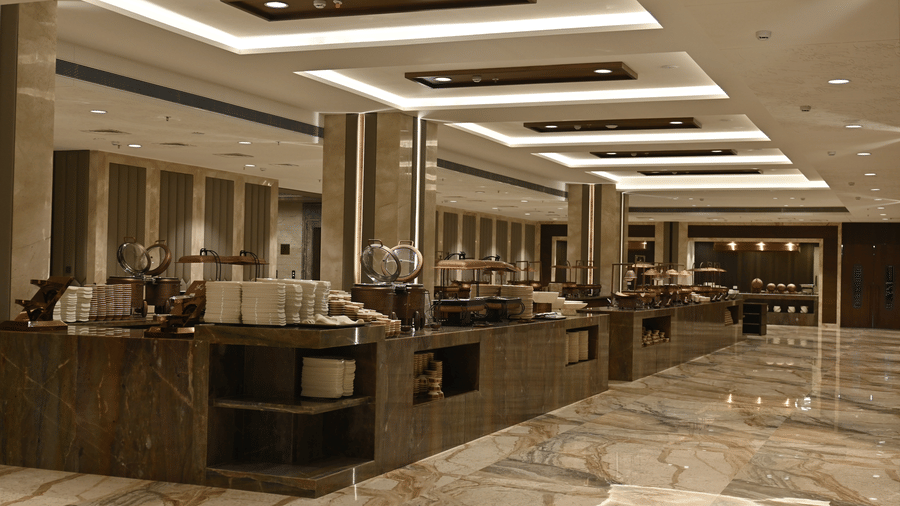 A spacious catering area features long service tables under a modern recessed ceiling in the Marquis banquet hall at Praveg's Grand Eulogia, Ahmedabad.