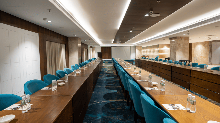 Perspective view of a long wooden meeting table with teal chairs and professional place settings - Praveg's Grand Eulogia, Ahmedabad