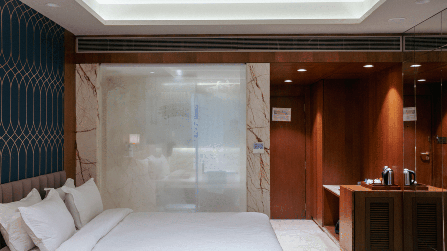 A contemporary hotel room featuring warm wood paneLling, a white bed, and sleek minimalist lighting - Praveg's Grand Eulogia, Ahmedabad