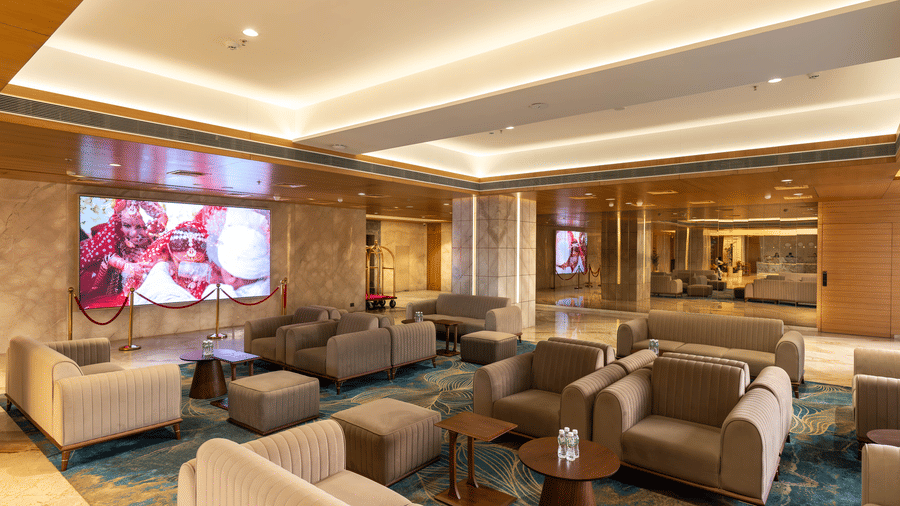 A contemporary guest lounge with plush beige sofas, a large digital screen, and stylish interior decor - Praveg's Grand Eulogia, Ahmedabad