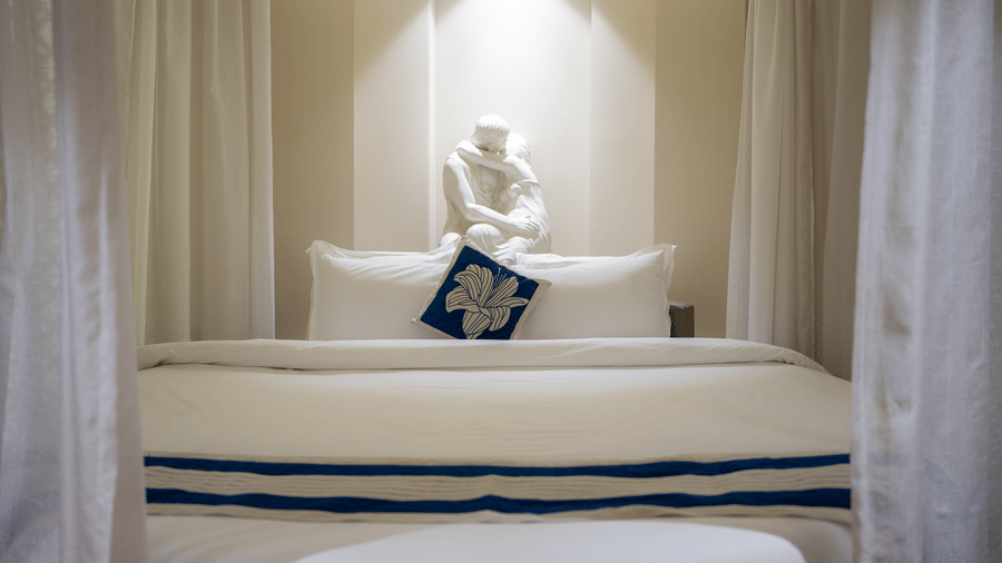 A serene bedroom view with a comfortable bed, white linens, and decorative spiritual wall art - Praveg's Grand Eulogia, Ahmedabad