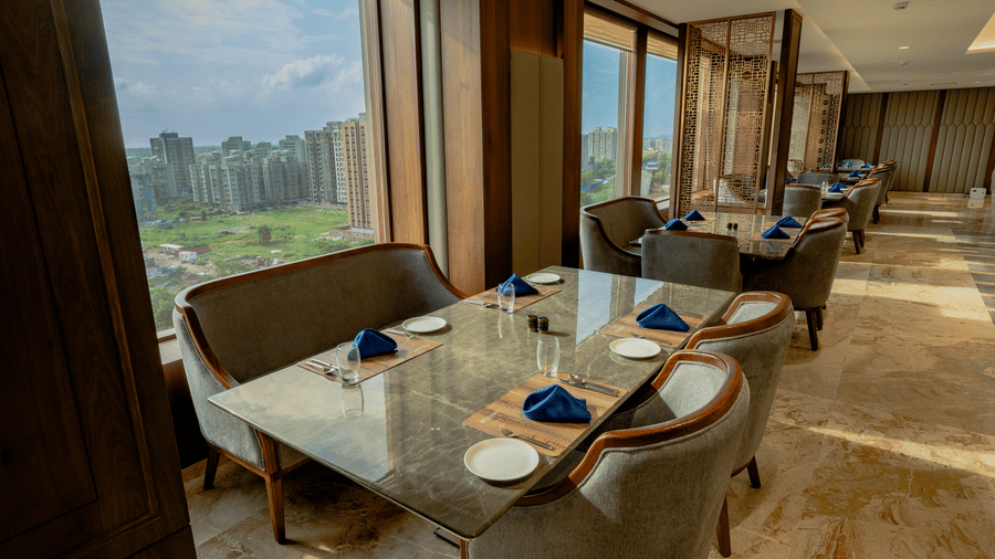 Elegant restaurant seating next to large windows offering a scenic view of the city skyline - Praveg's Grand Eulogia, Ahmedabad