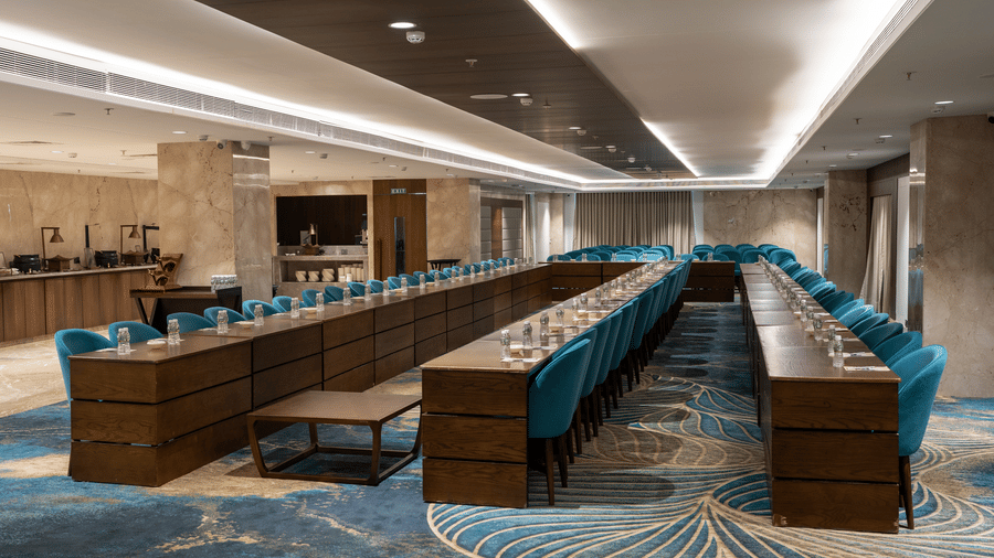 A large boardroom arranged in a U-shape with blue chairs and a floral patterned carpet - Praveg's Grand Eulogia, Ahmedabad