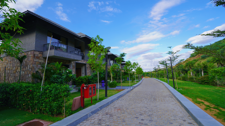 A long pathway leading to the resort villas, bordered by a green lawn and trees.