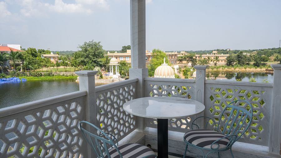 A cosy balcony with a round coffee table and chairs overlooking a water body - Rajbagh Wellness, Udaipur