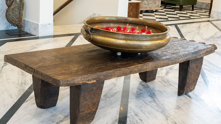 An image of a vessel with petals and water placed on a wooden table at Rajbagh Wellness