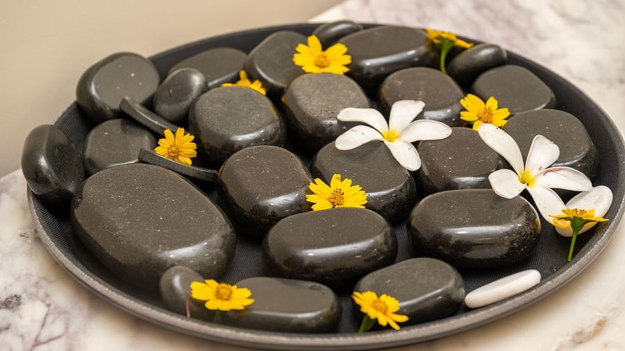 An image of plate where several massage stones are placed along with flowers at Rajbagh Wellness