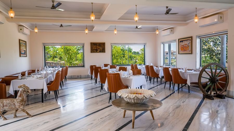 An image of our cosy restaurant surrounded by lush greenery seen from the windows - Rajbagh Wellness, Udaipur