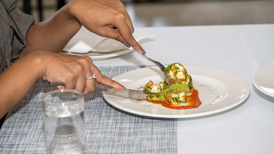 A woman cutting into a dish with a knife and fork at our restaurant - Rajbagh Wellness, Udaipur