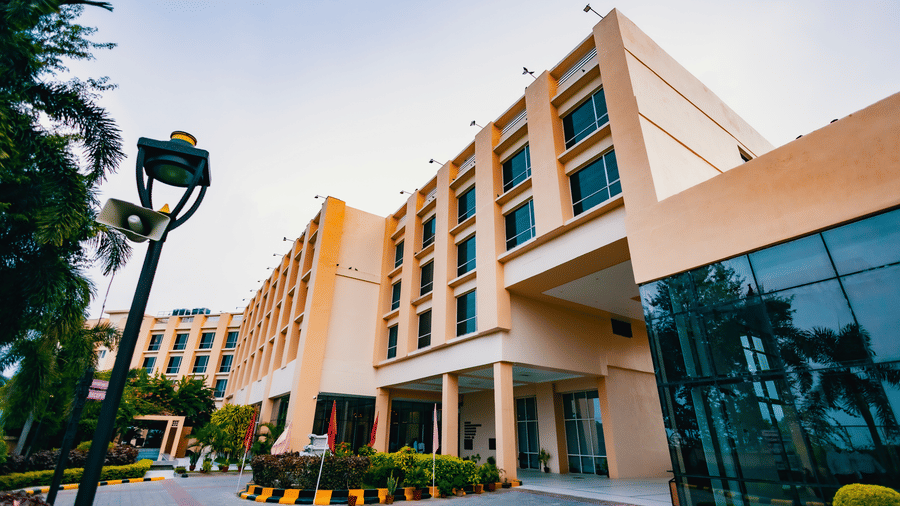 A modern hotel exterior at Ramada by Wyndham Bodh Gaya Mahabodhi, featuring a glass entrance and is seen under clear daylight.