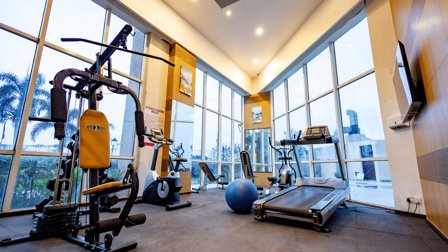 A brightly lit gymnasium with large windows showcasing various pieces of cardio equipment at Ramada by Wyndham Bodh Gaya Mahabodhi.