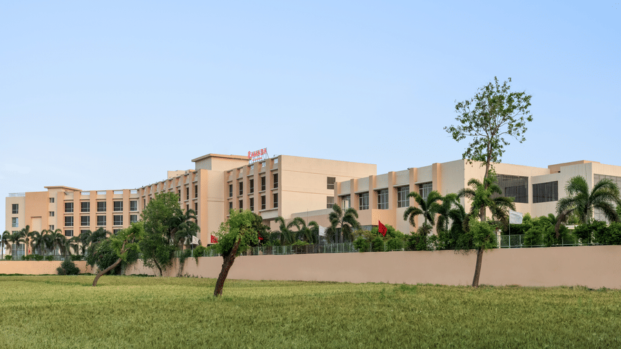 Exterior of Ramada by Wyndham Bodh Gaya Mahabodhi featuring a well-manicured lawn with some plants, and the facade of the hotel in the background.