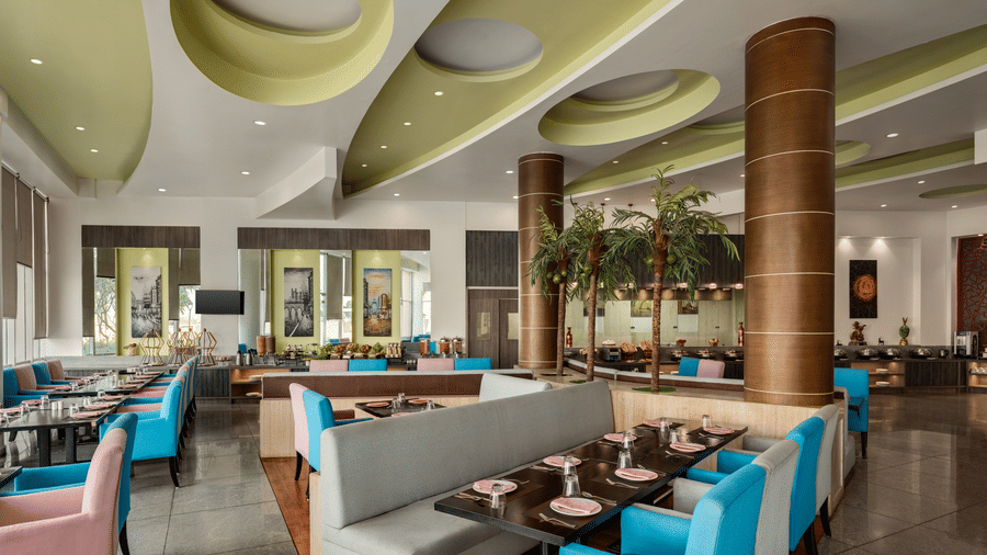 The indoor dining area of Jalpaan coffee shop at Ramada by Wyndham Bodh Gaya Mahabodhi features neatly arranged tables and comfortable booths.