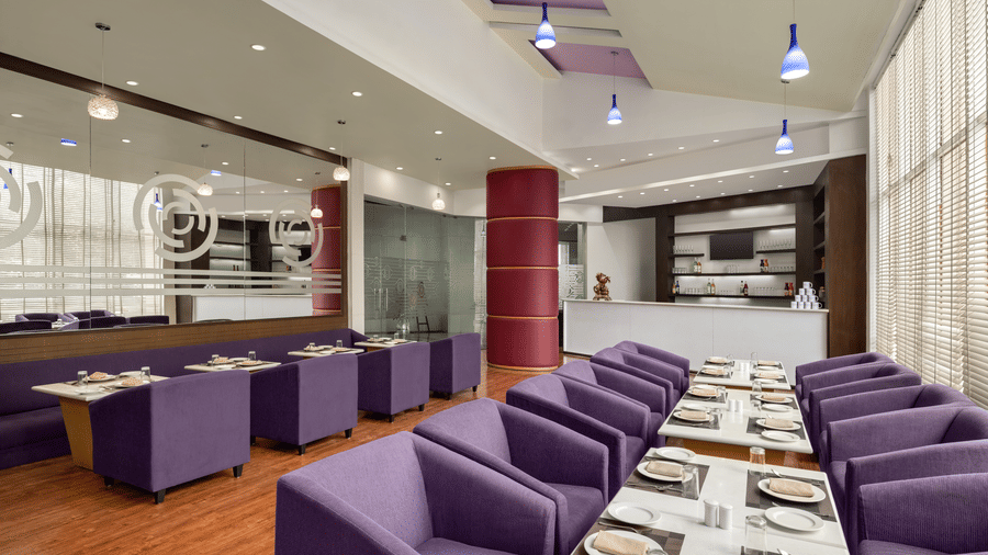 The Maya lounge at Ramada by Wyndham Bodh Gaya Mahabodhi featuring rows of neatly arranged tables and chairs with elegant modern interiors.