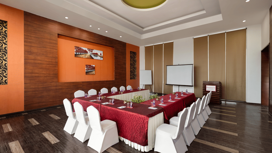 The Shubham meeting room at Ramada by Wyndham Bodh Gaya Mahabodhi displays an organised cluster of tables and chairs for event guests.