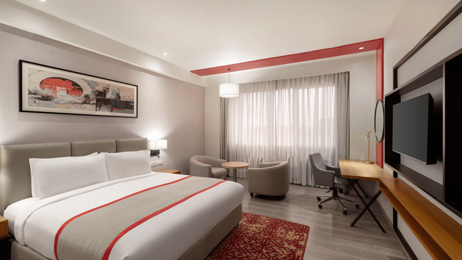Standard King Room at Ramada by Wyndham Bodh Gaya Mahabodhi featuring a neatly made king size bed, a wall-mounted television, a rug under the bed, and a seating area.