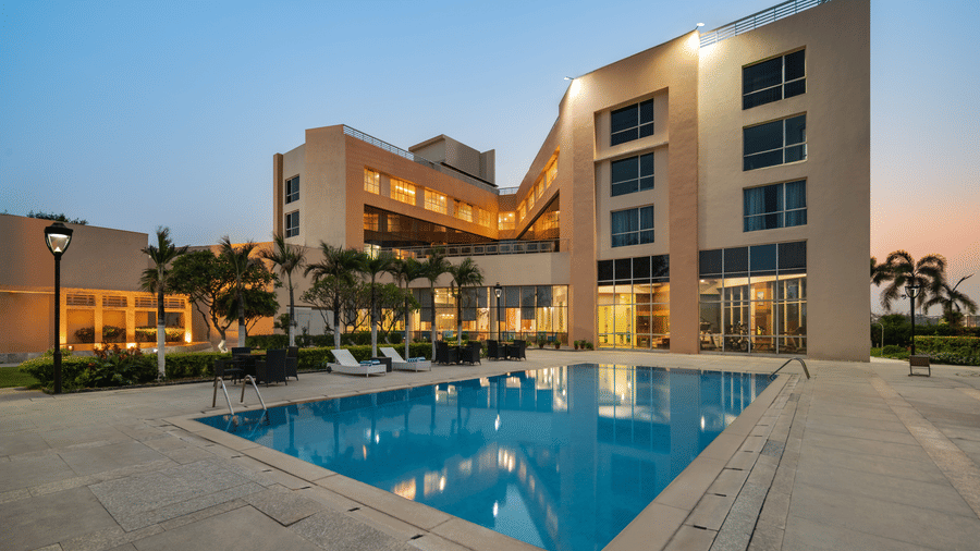 Swimming pool area of Ramada by Wyndham Bodh Gaya Mahabodhi featuring a deck, the pool and the lit facade of the building in the background. 