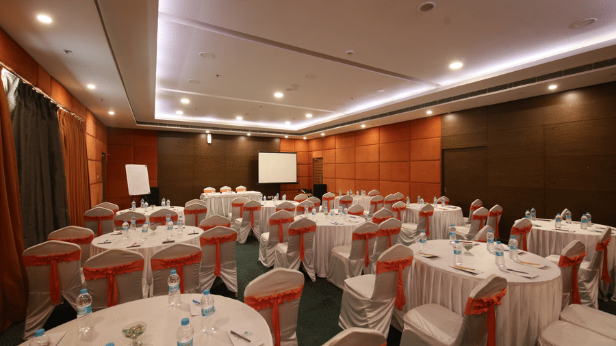 A spacious banquet hall set up with round tables, white tablecloths, and red chair sashes - Ramada by Wyndham Bodh Gaya Mahabodhi 