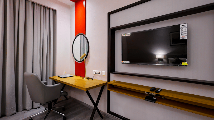 A stylish room with a wall-mounted television, desk, and a distinctive round mirror - Ramada by Wyndham Bodh Gaya Mahabodhi